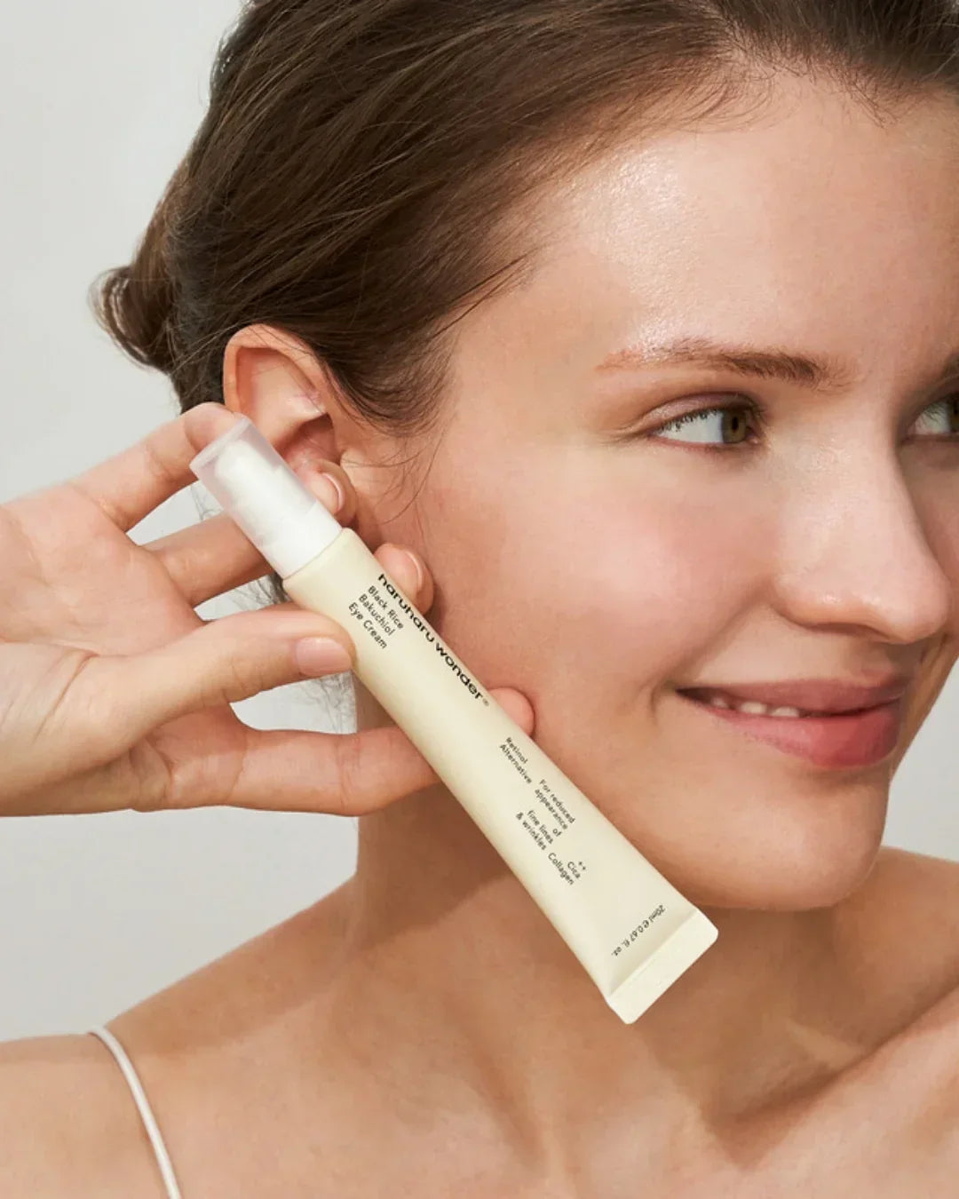 Woman holding Naturopathica Black Rice Bakuchiol eye cream tube near her face with smooth skin