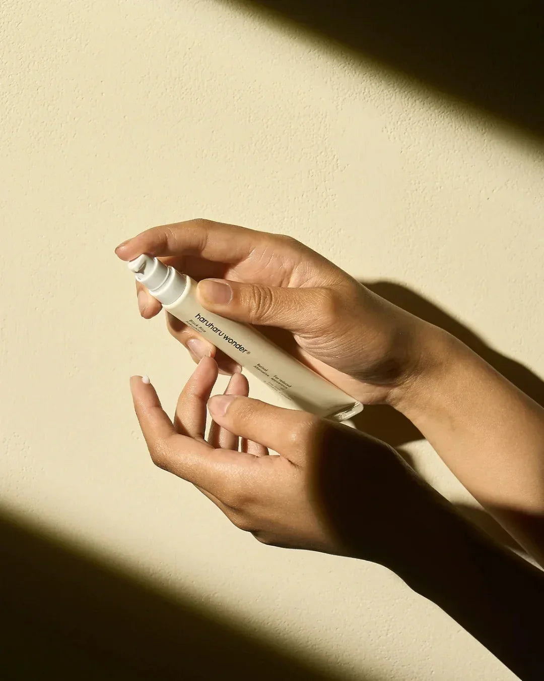 Hands holding and dispensing Haruharu Wonder Black Rice Bakuchiol Eye Cream with texture visible on fingertip