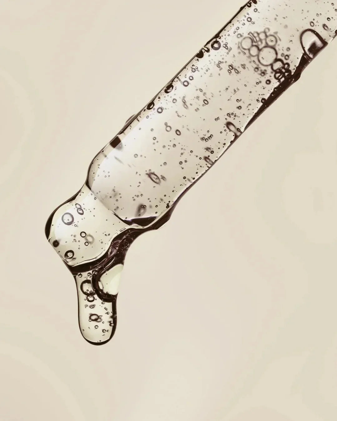 Close-up of a transparent dropper with clear serum and bubbles against a beige background