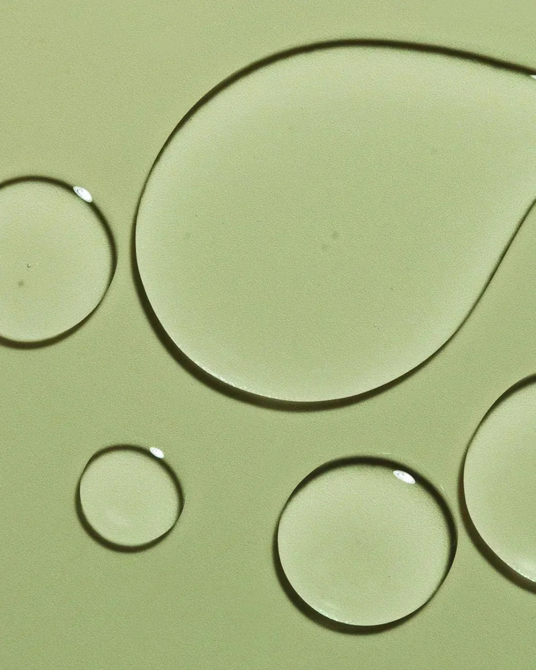 Close-up of clear water droplets on pale green surface, highlighting hydrating skincare texture