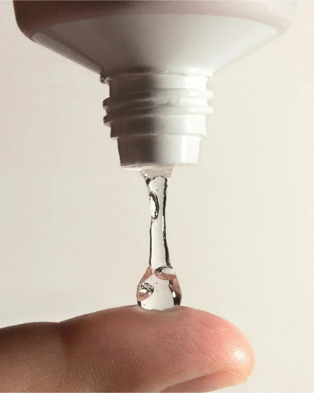 Clear gel dripping from white tube onto finger, showcasing smooth texture and moisture