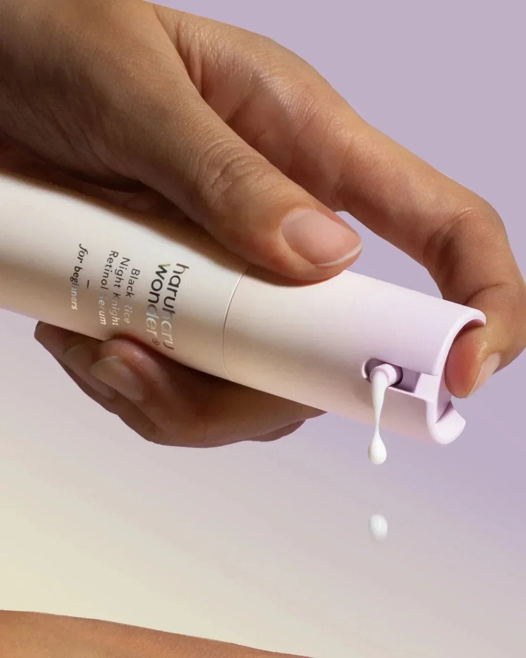Hand dispensing Haruharu Wonder Black Rice Night Knight retinol serum lotion against purple background