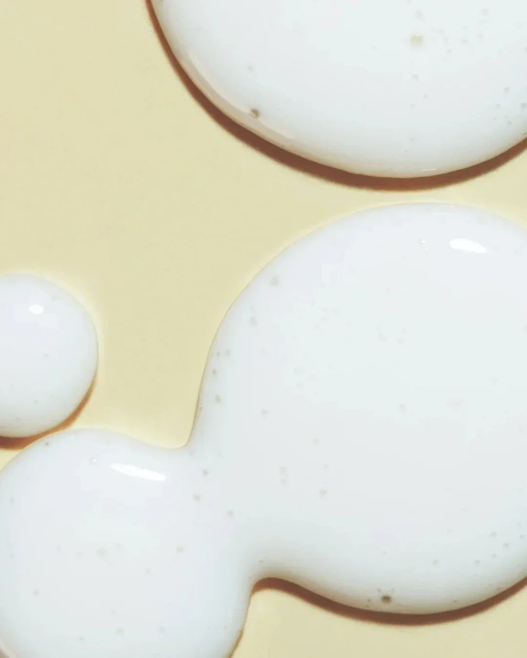 Close-up of white creamy skincare essence texture with tiny bubbles on beige background