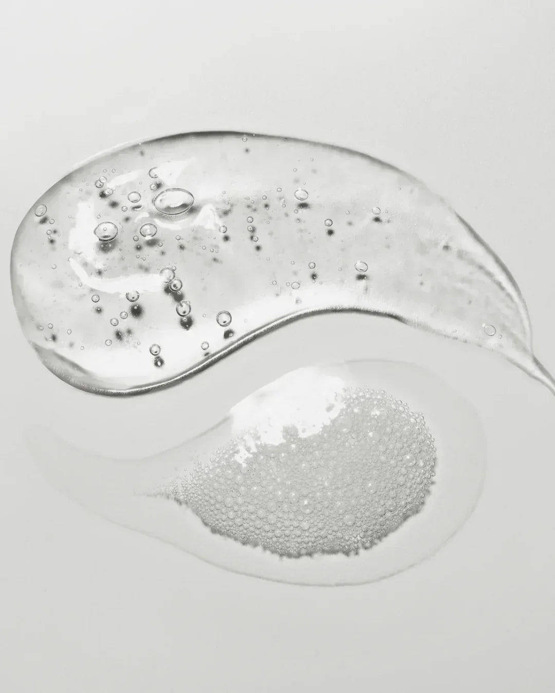 Close-up of two clear gel drops with bubbles representing skincare cleansing gel texture