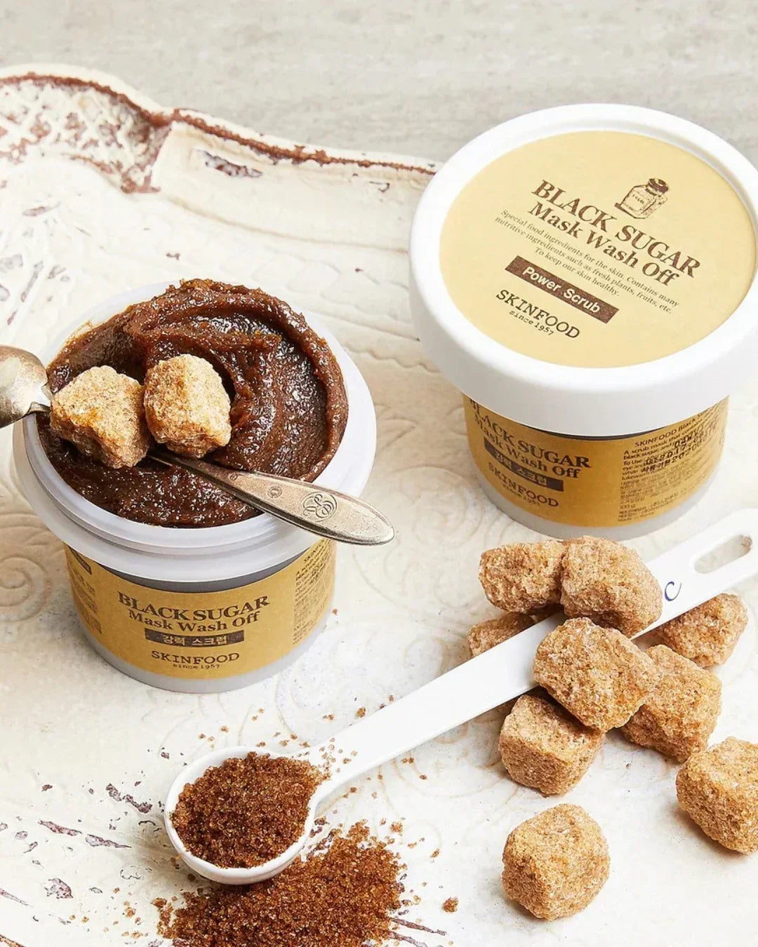 Skinfood Black Sugar Mask Wash Off scrub in open jar with brown sugar chunks and granules on white surface