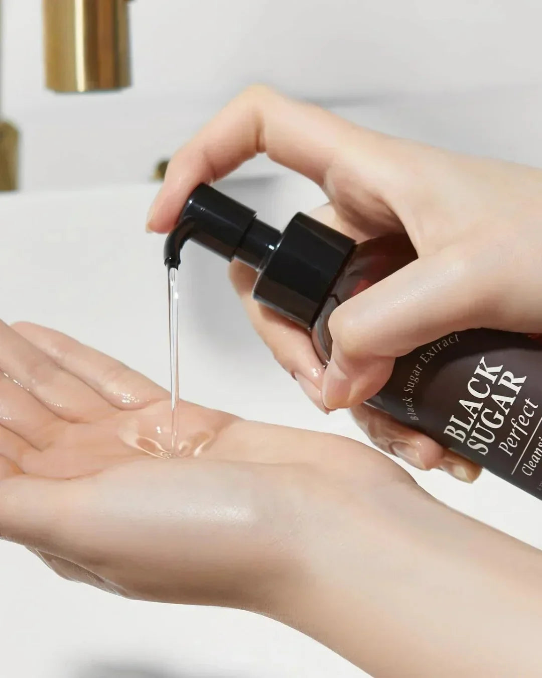 Hand dispensing Black Sugar Perfect Cleansing Oil into palm over white sink with gold faucet