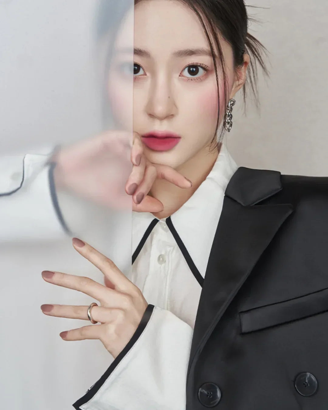 Close-up of woman with pink lipstick and blush wearing black blazer and white shirt, holding frosted glass