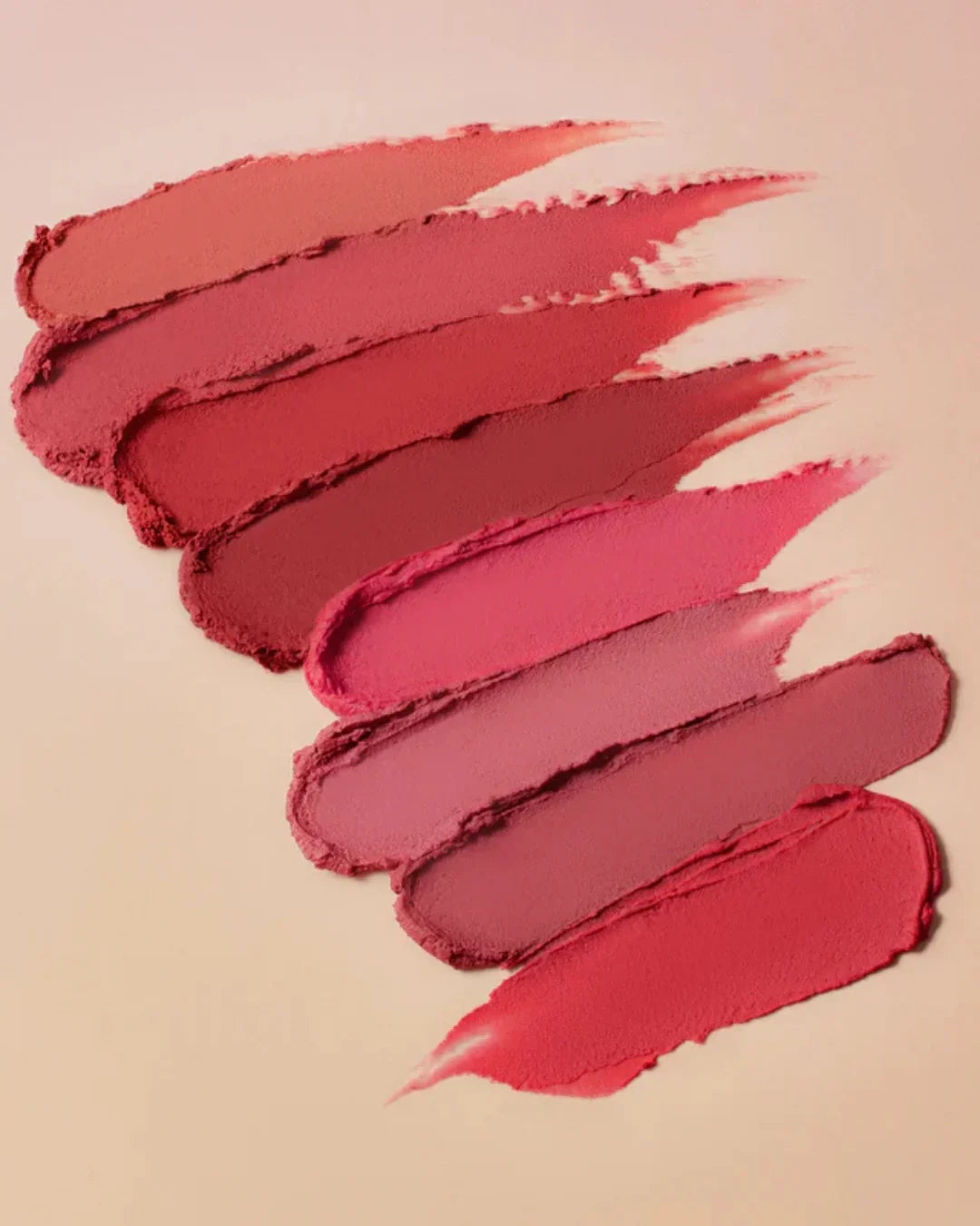 Swatches of creamy matte lipstick in various pink and red shades on beige background