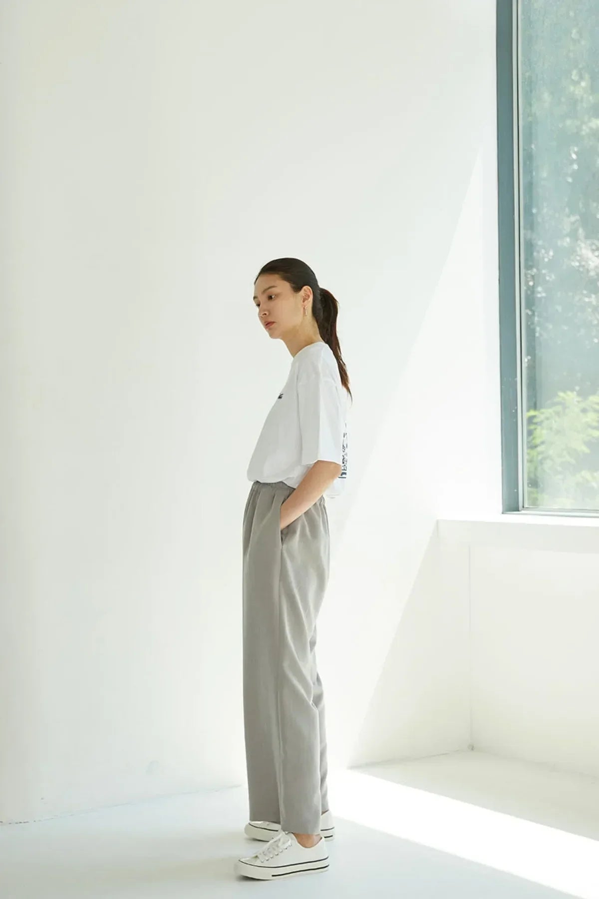 Woman in white Bongsan mask dance T-shirt and gray pants standing in a bright room by a window