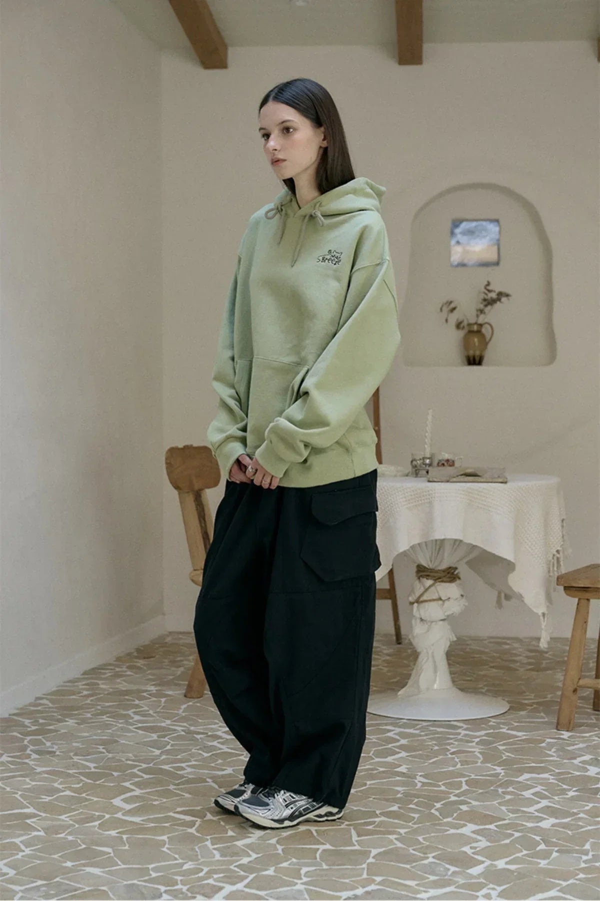 Woman wearing khaki Breezecat embroidered hoodie and black wide cargo pants indoors