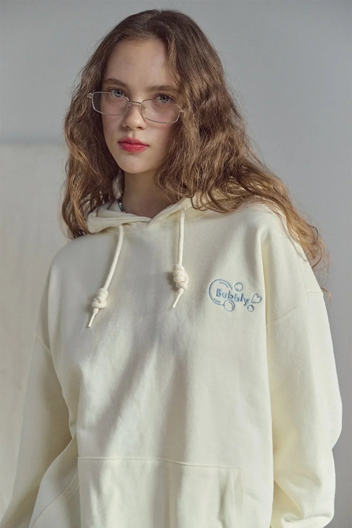 Young woman wearing cream hoodie with bubbly embroidered design and drawstrings, natural light