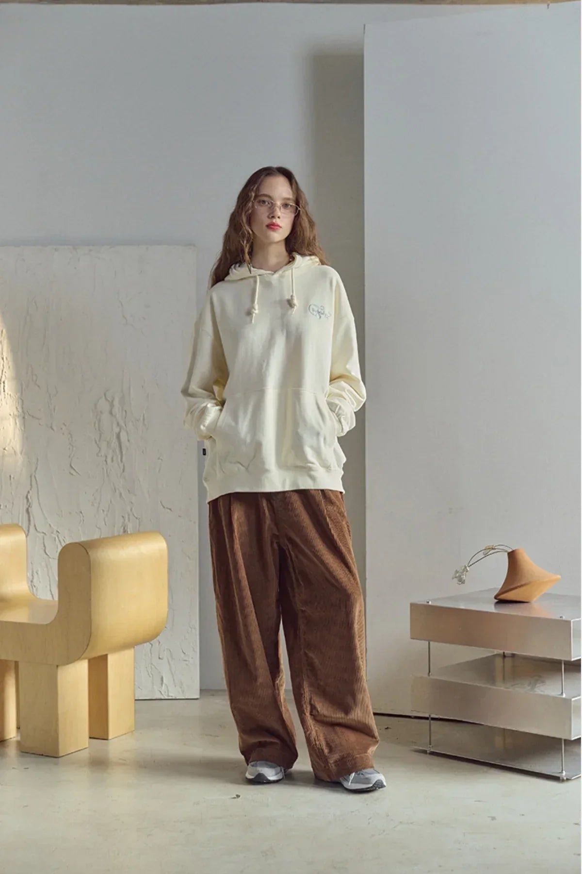 Young woman wearing cream embroidered hoodie and brown wide pants in minimalist indoor setting