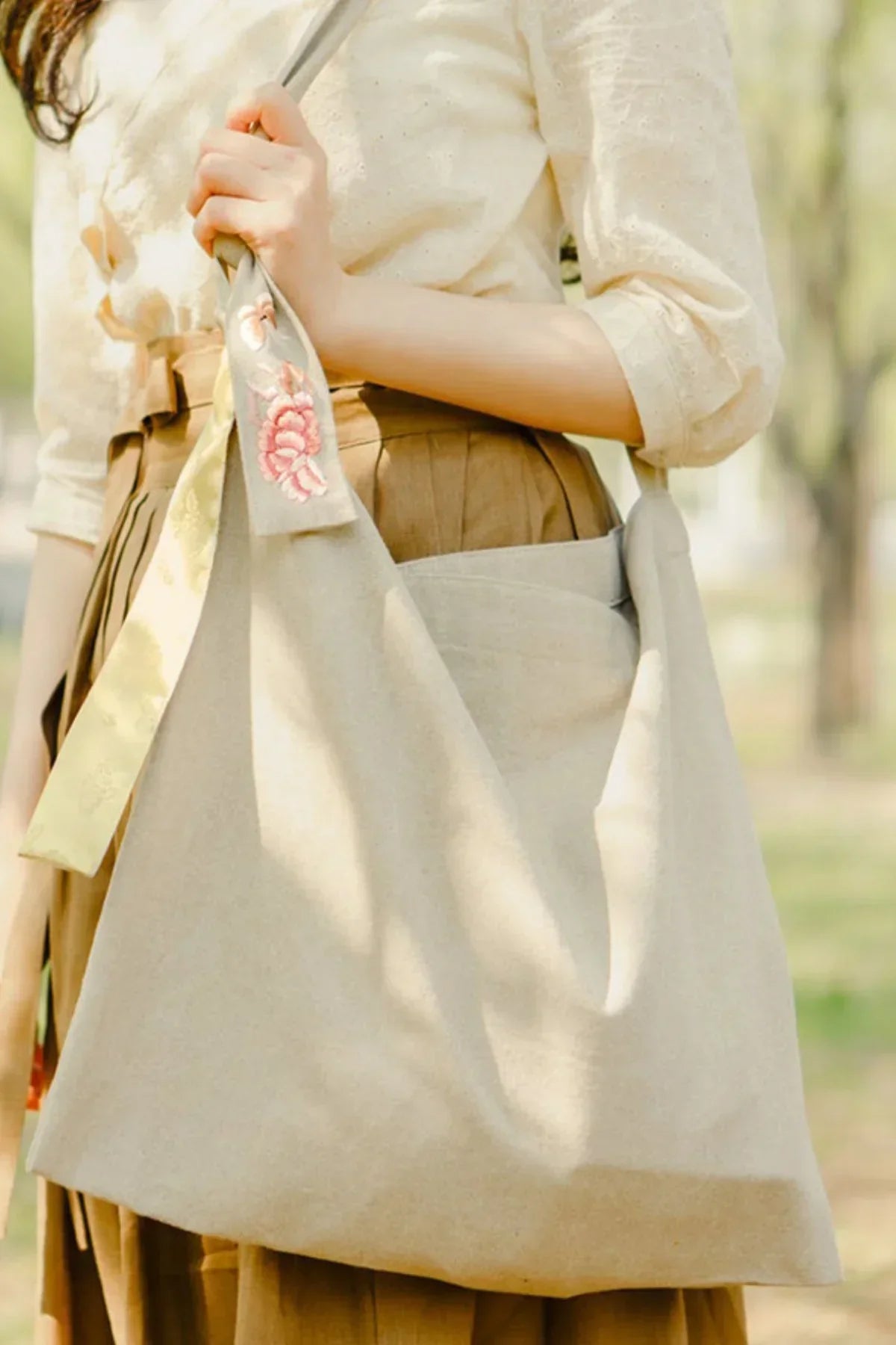 Beige butterfly daily tote bag with floral embroidery held by woman in cream blouse and brown skirt