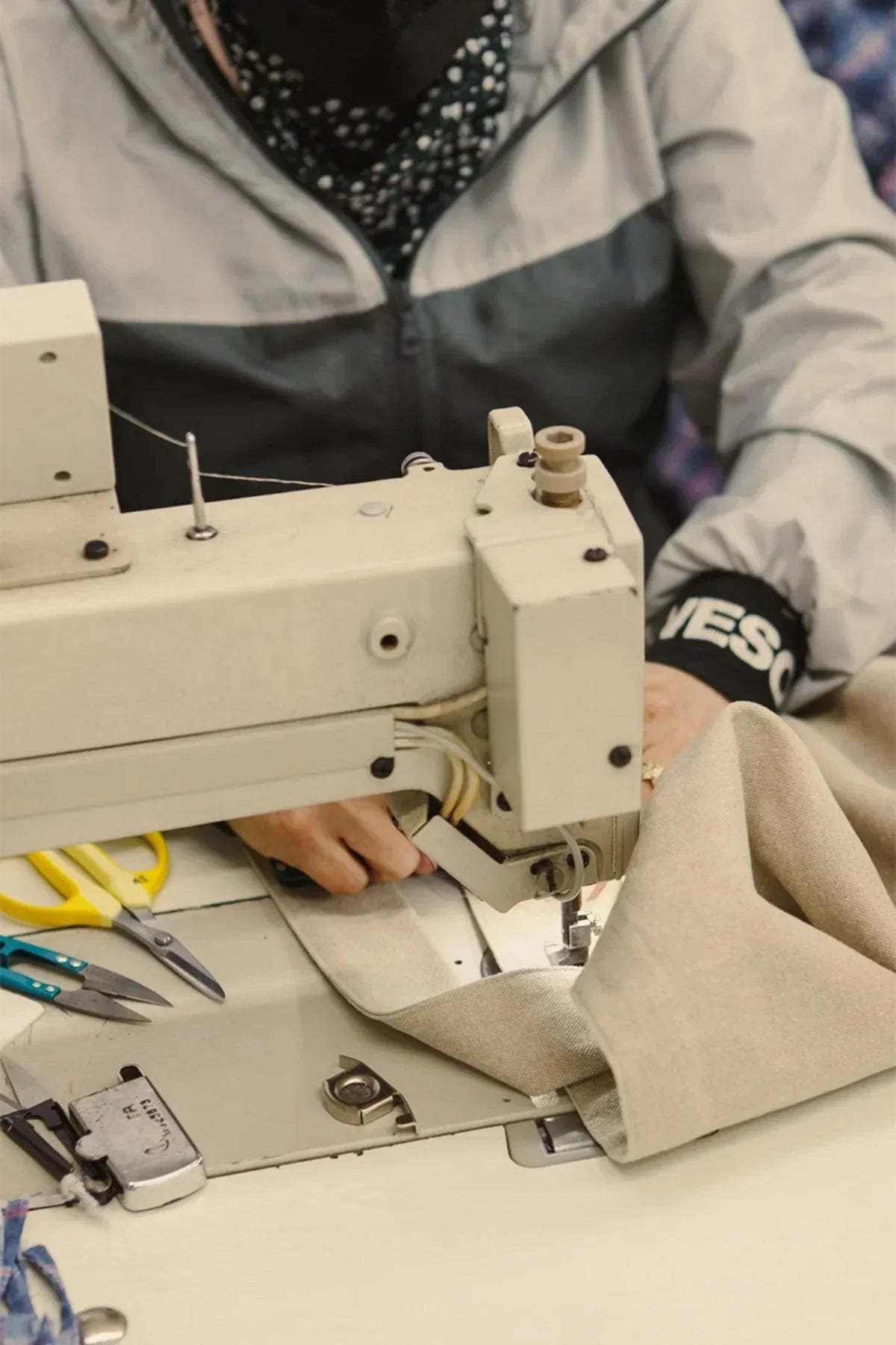 Close-up of a person sewing beige fabric with an industrial sewing machine in a workshop