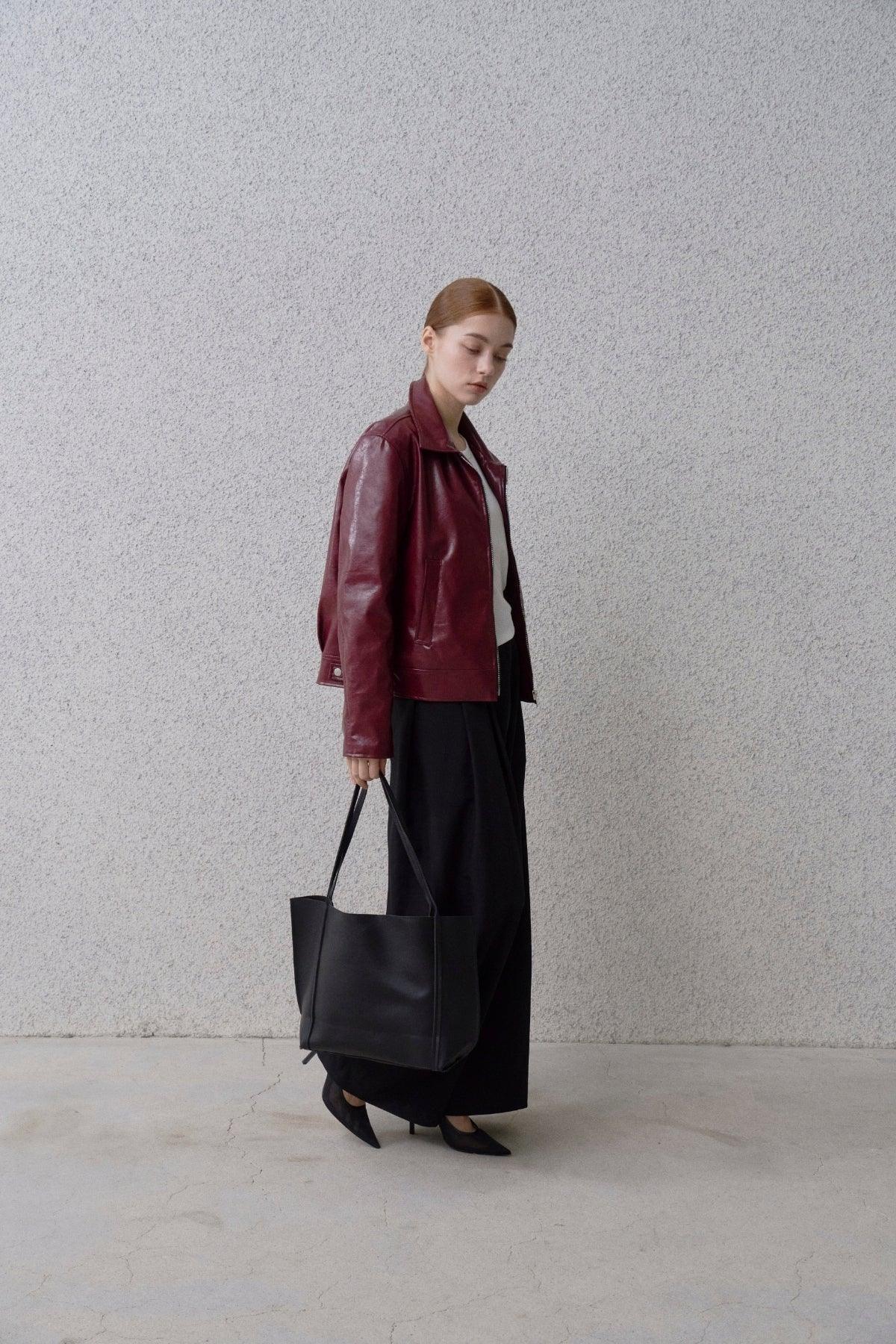 Woman wearing black wide-fit pants, burgundy leather jacket, black heels, and carrying large black tote bag