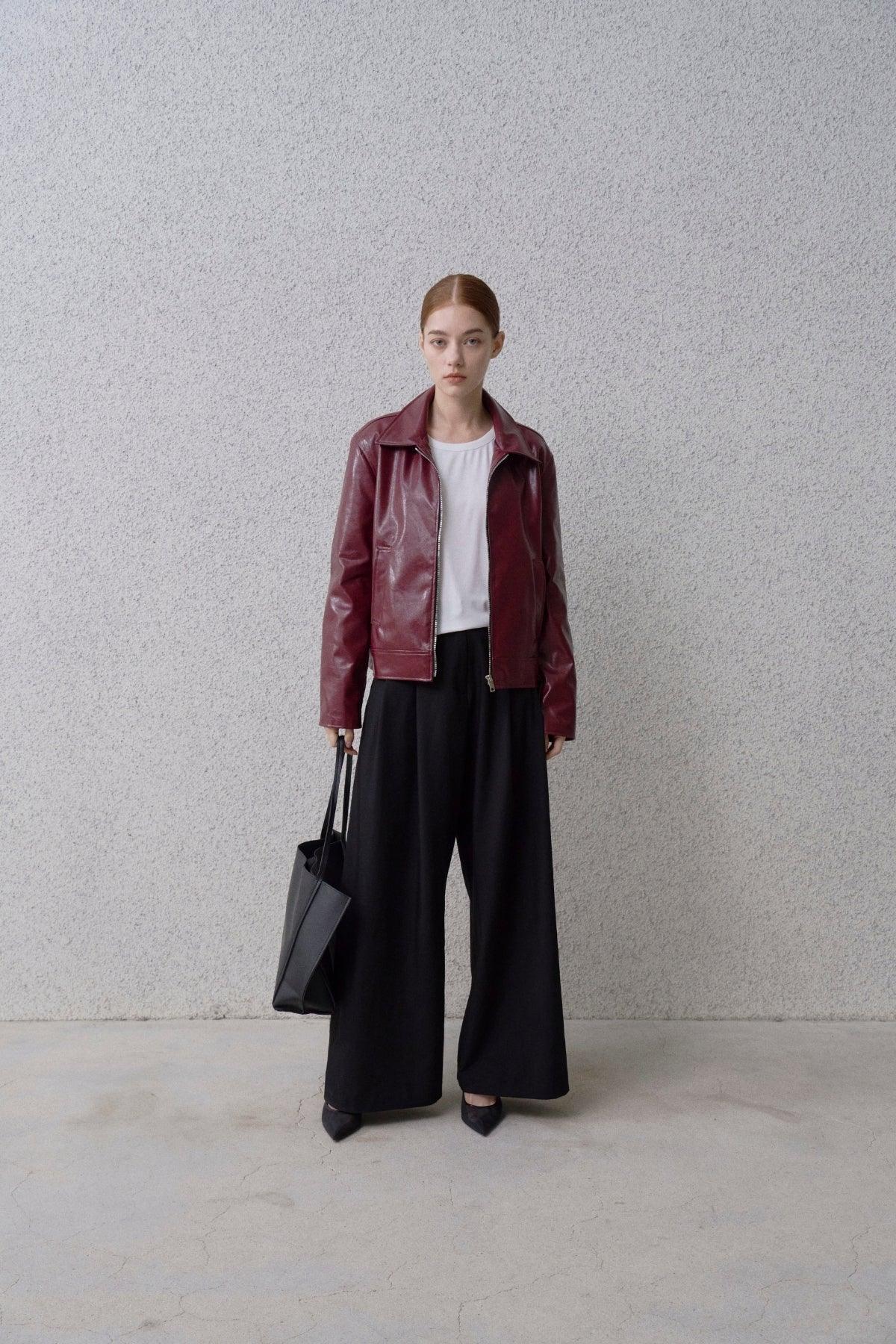 Woman wearing burgundy leather jacket, white top, wide black pants, black heels, holding black tote bag