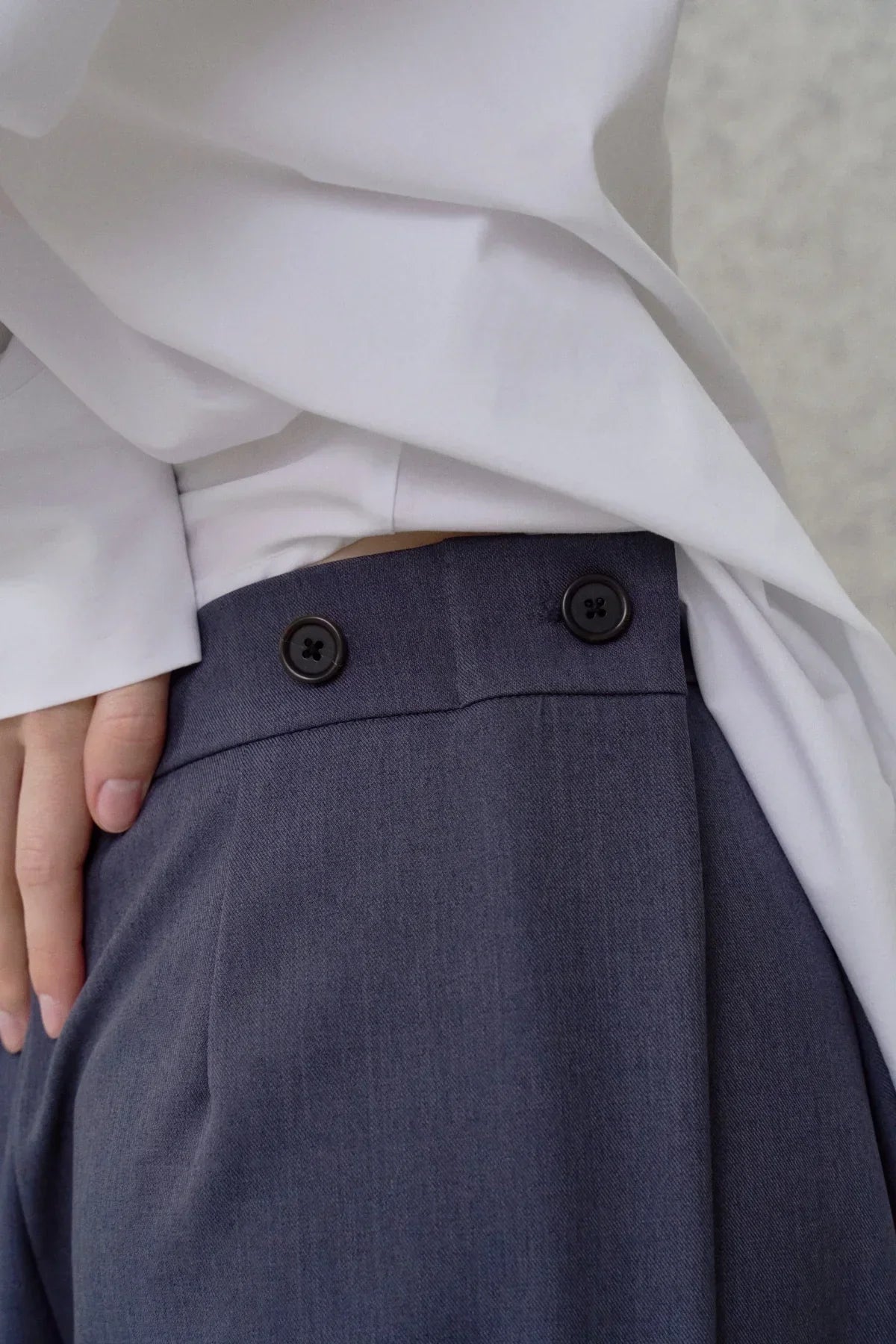 Close-up of blue wide fit pants with button details worn with a white tucked-in shirt