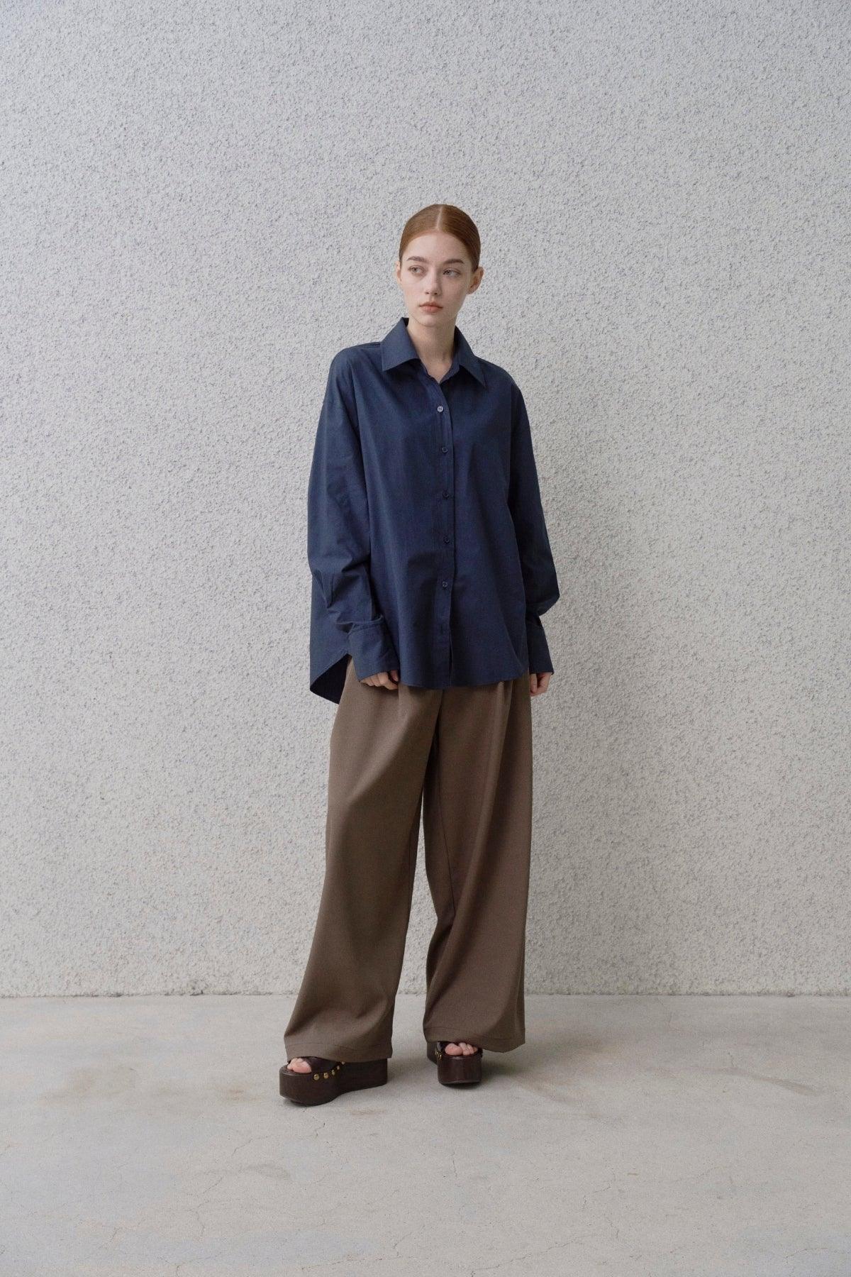Woman in navy oversized shirt and brown wide-leg pants with platform sandals against gray textured wall