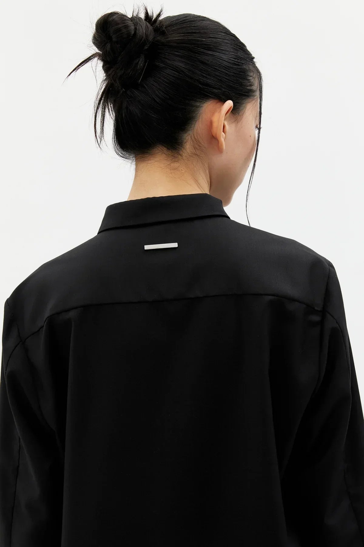 Close-up of a woman wearing a black buttonless shirt with a small horizontal metal detail on the back collar