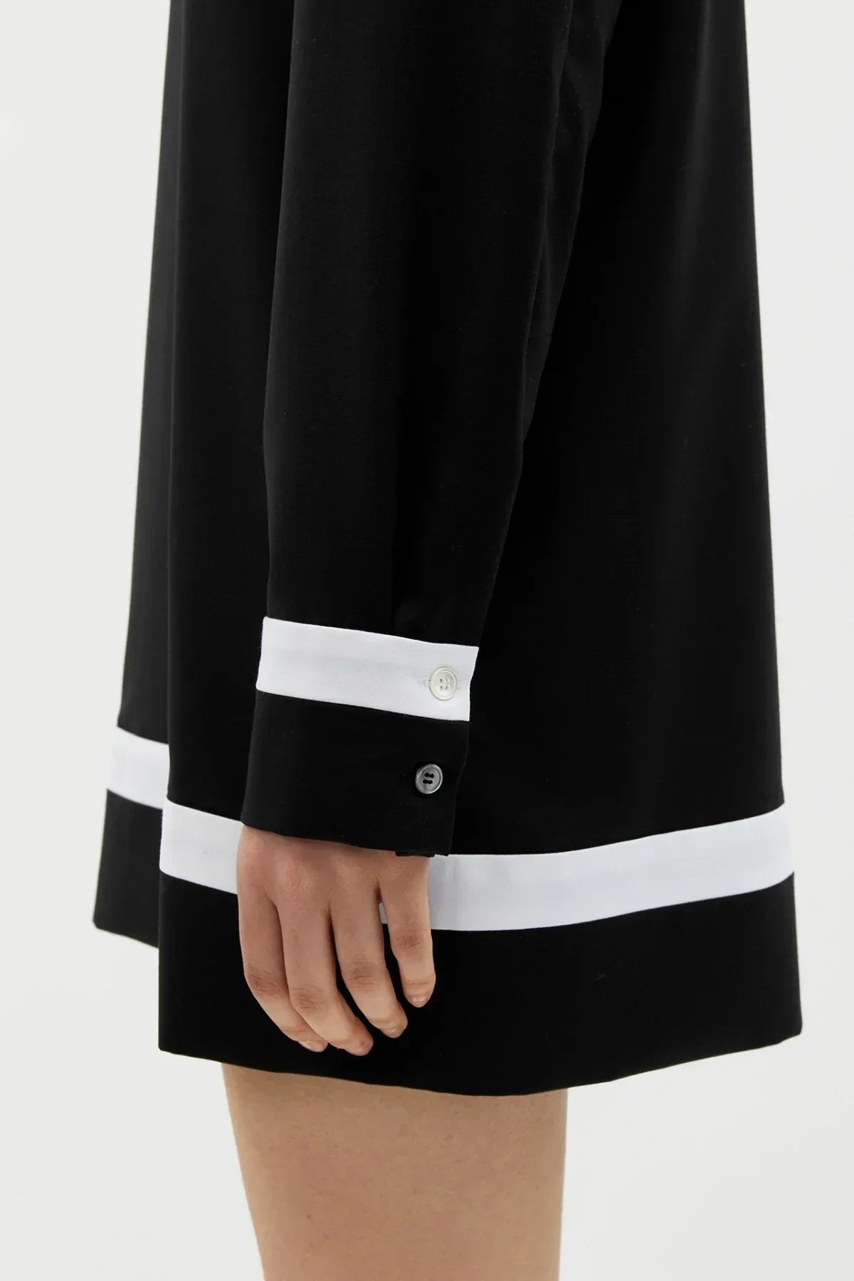Close-up of a black long-sleeve dress with white cuffs and hem, worn by a person