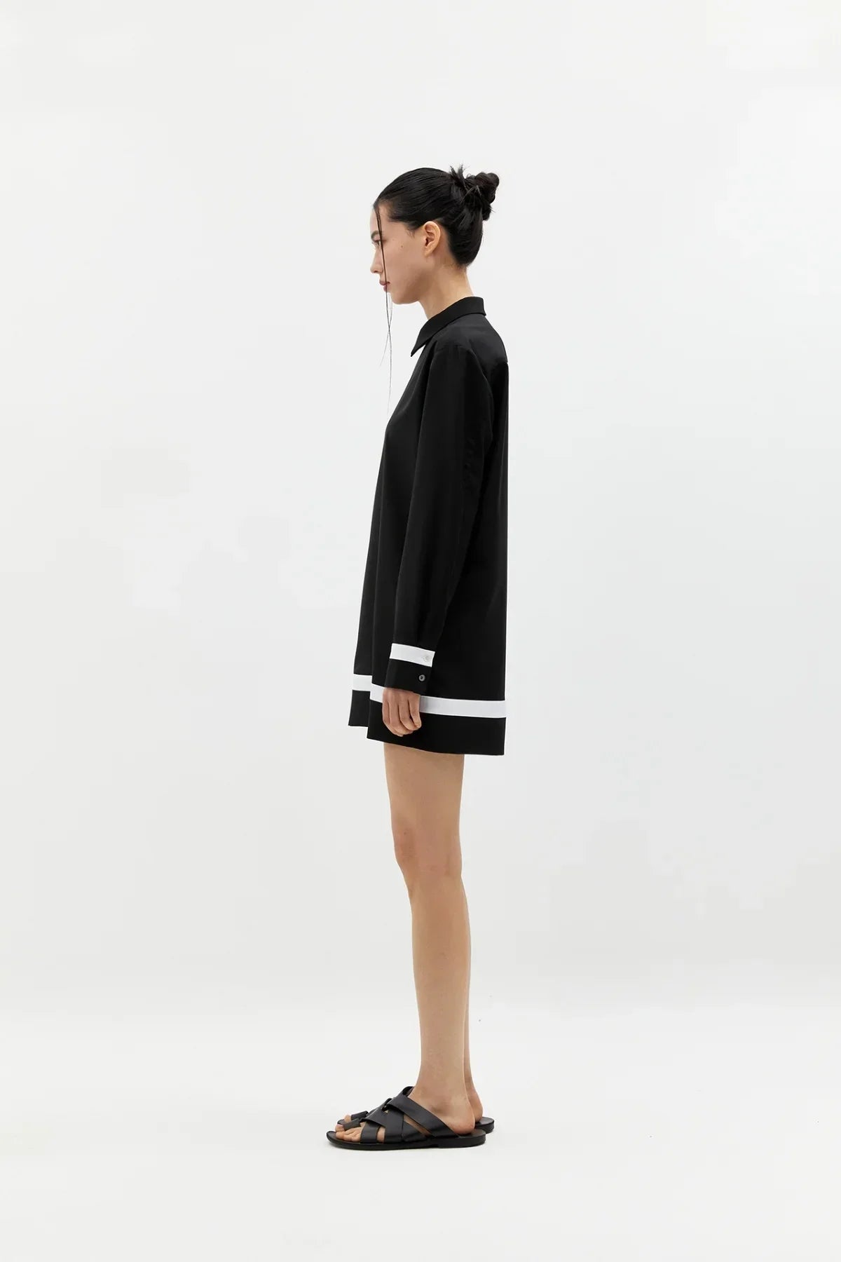 Side view of woman wearing black buttonless long-sleeve shirt dress with white trim and black sandals
