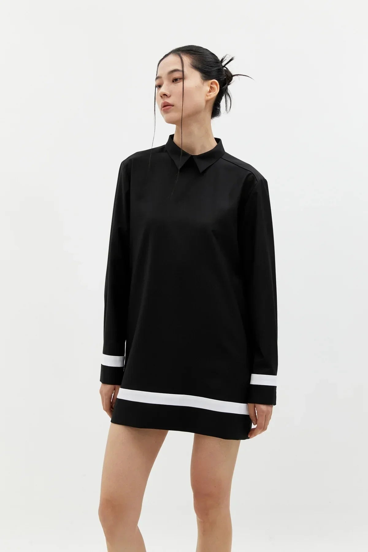 Woman wearing a black buttonless shirt dress with white stripes on sleeves and hem in studio