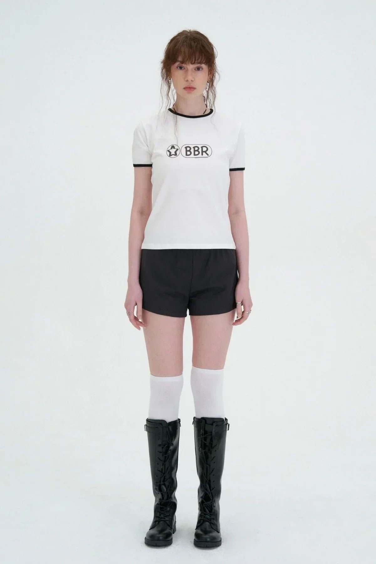 Model wearing white BBR graphic t-shirt, black shorts, knee-high white socks, and black lace-up boots