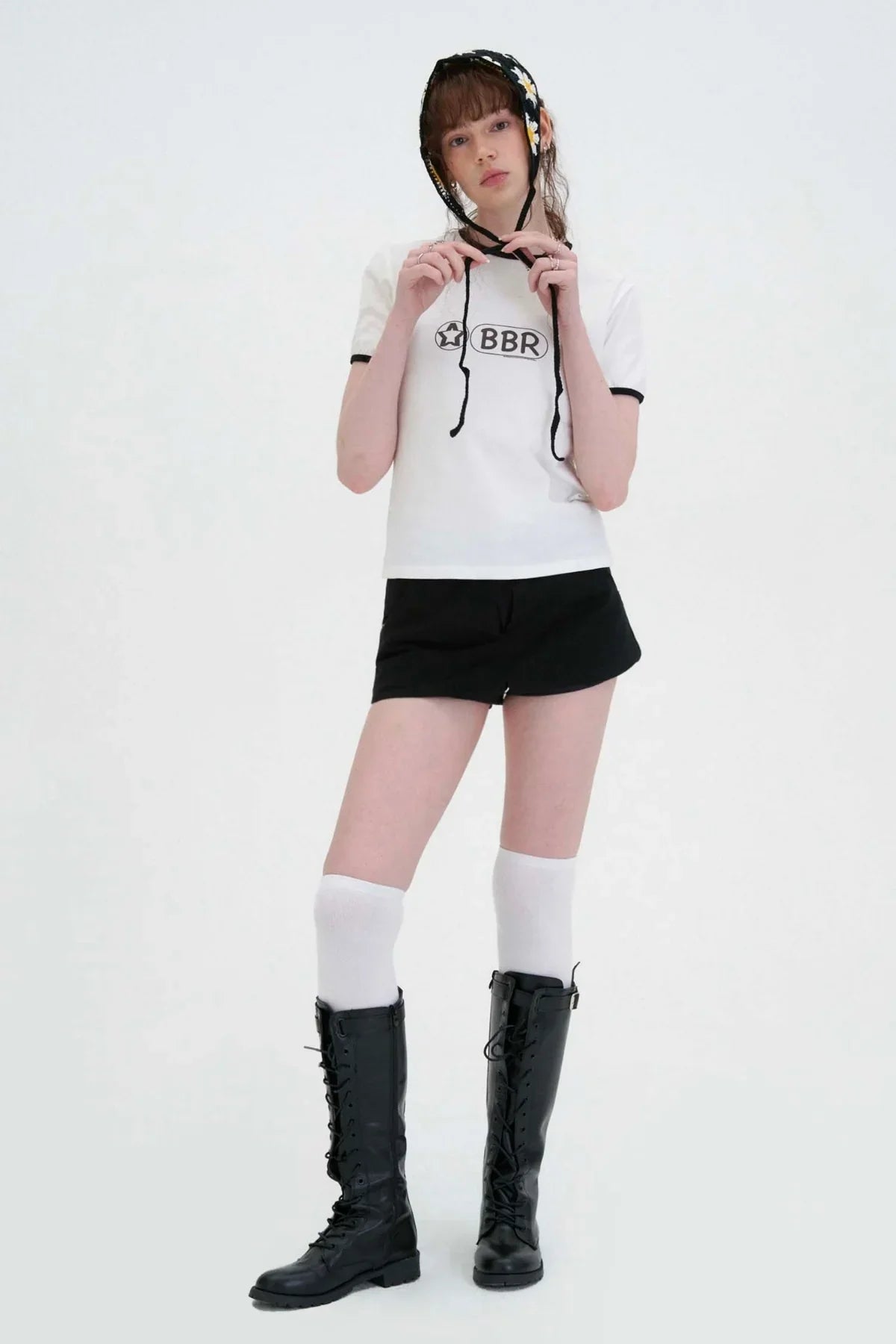 Model in black mini skirt, white graphic top, knee-high socks, and boots, styled for Korean fashion at Malkn