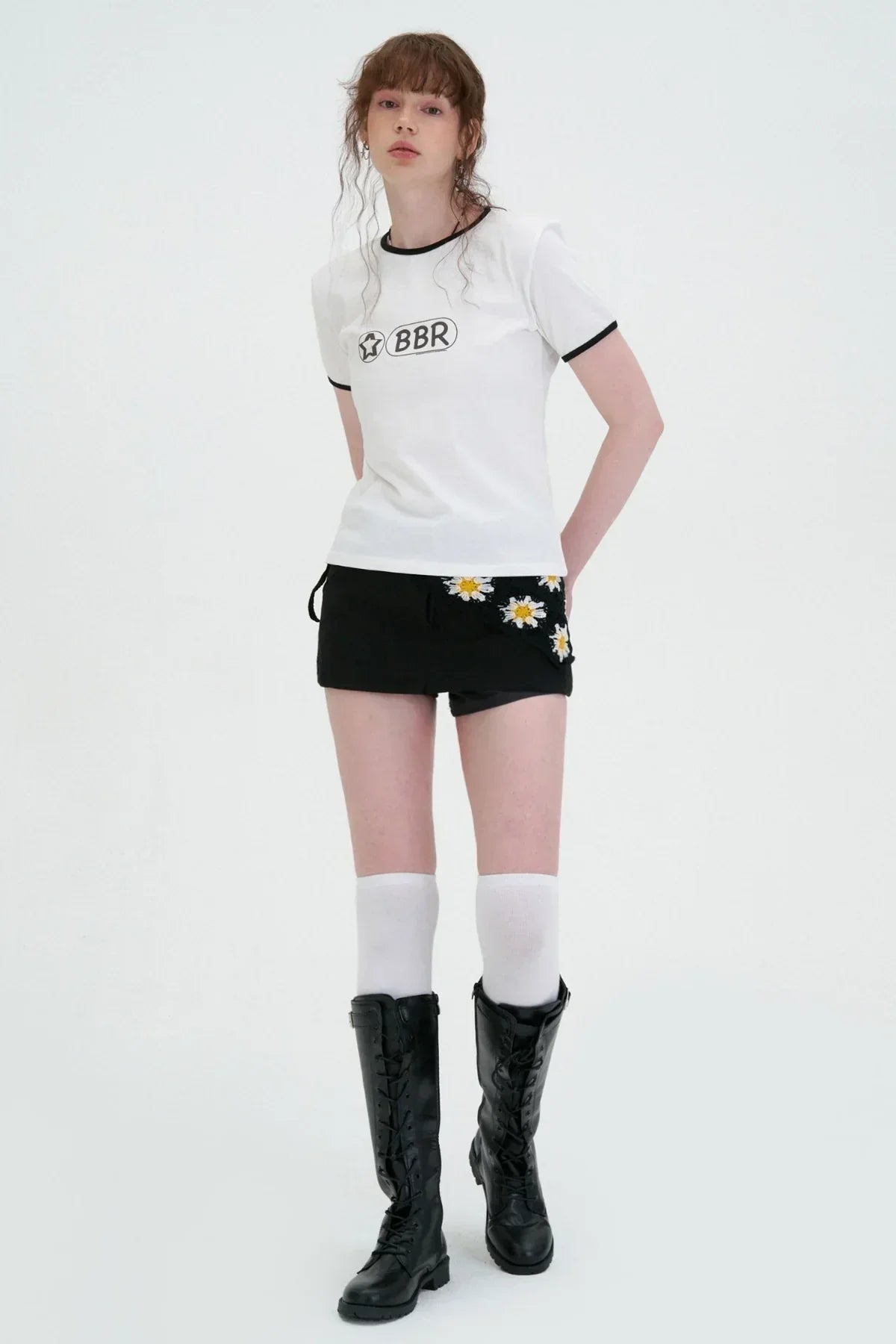 Model in a white BBR t-shirt and black mini skirt with daisy detail, knee-high socks, and boots, Korean fashion style, Malkn studio shoot.