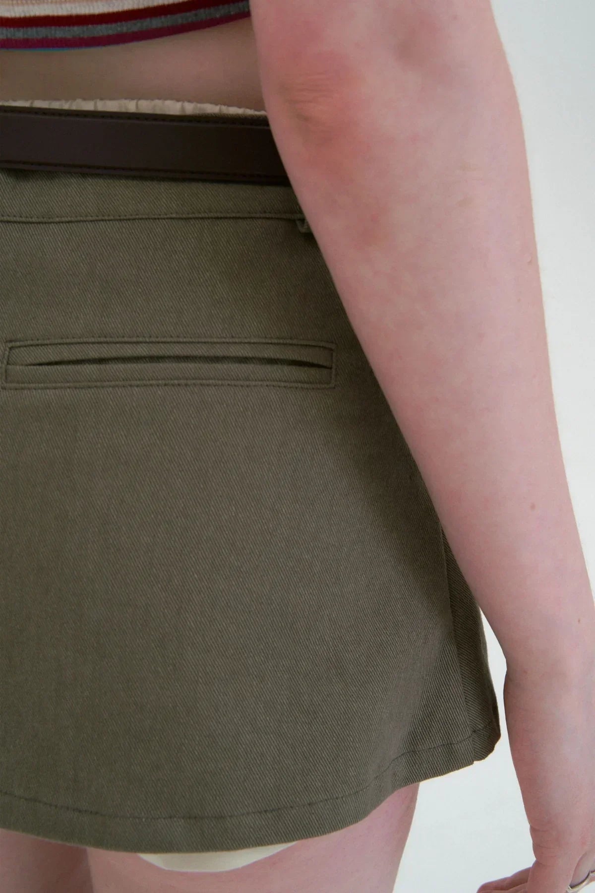Close-up of khaki double mini skirt with back pocket and brown belt on model