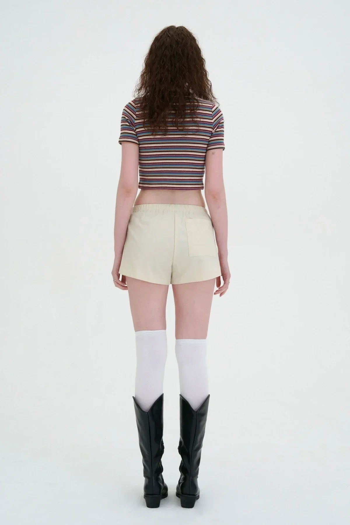 Woman wearing striped cropped top, khaki mini skirt, white knee-high socks, and black boots on white background