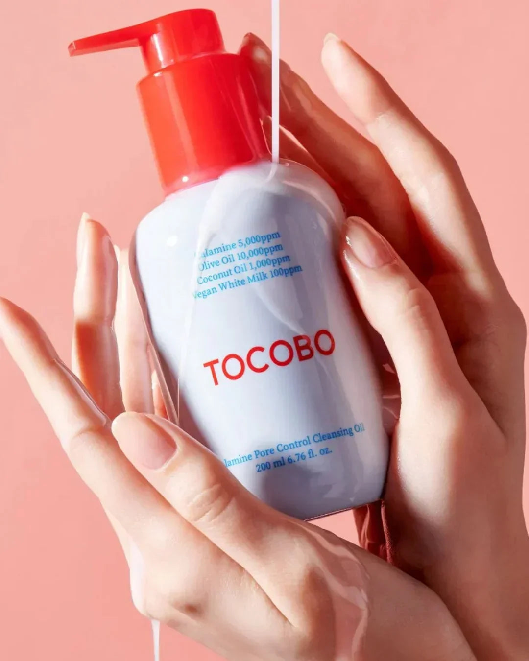 Hands holding Tocobo Calamine Pore Control Cleansing Oil bottle with red pump over pink background