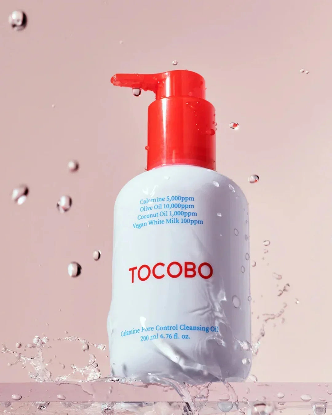 TOCOBO Calamine Pore Control Cleansing Oil bottle with red pump and water splashes on light pink background