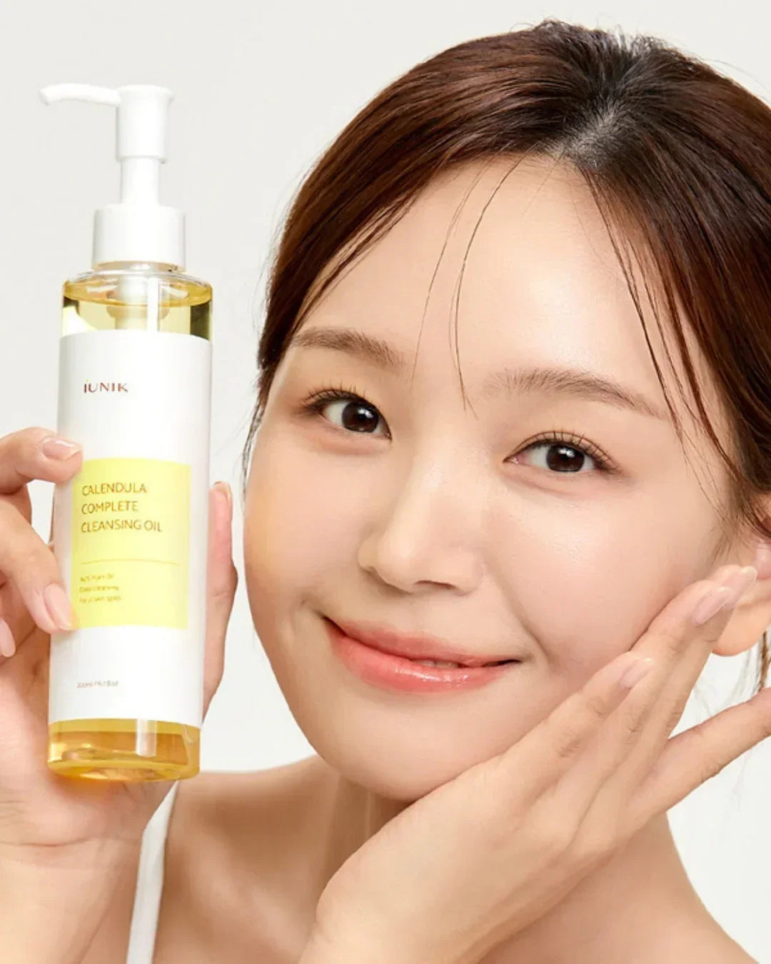 Smiling woman holding iUNIK Calendula Complete Cleansing Oil bottle showing clear skin and gentle skincare