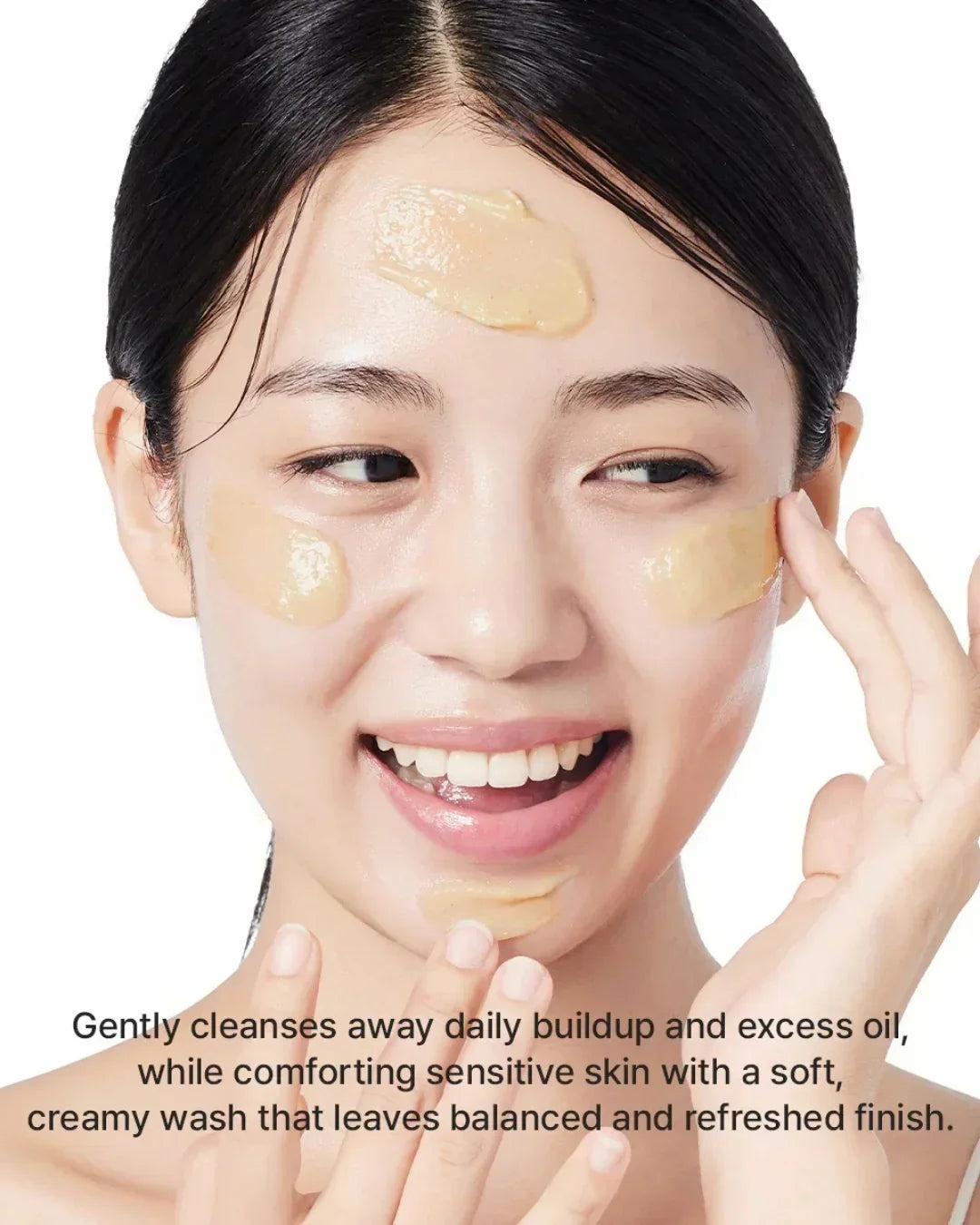 Young woman smiling with creamy yellow cleanser applied on forehead, cheeks, and chin for skincare