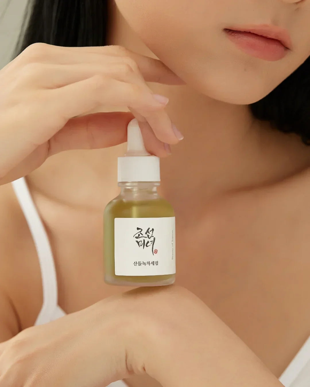 Close-up of woman holding green tea calming serum bottle with dropper for skincare