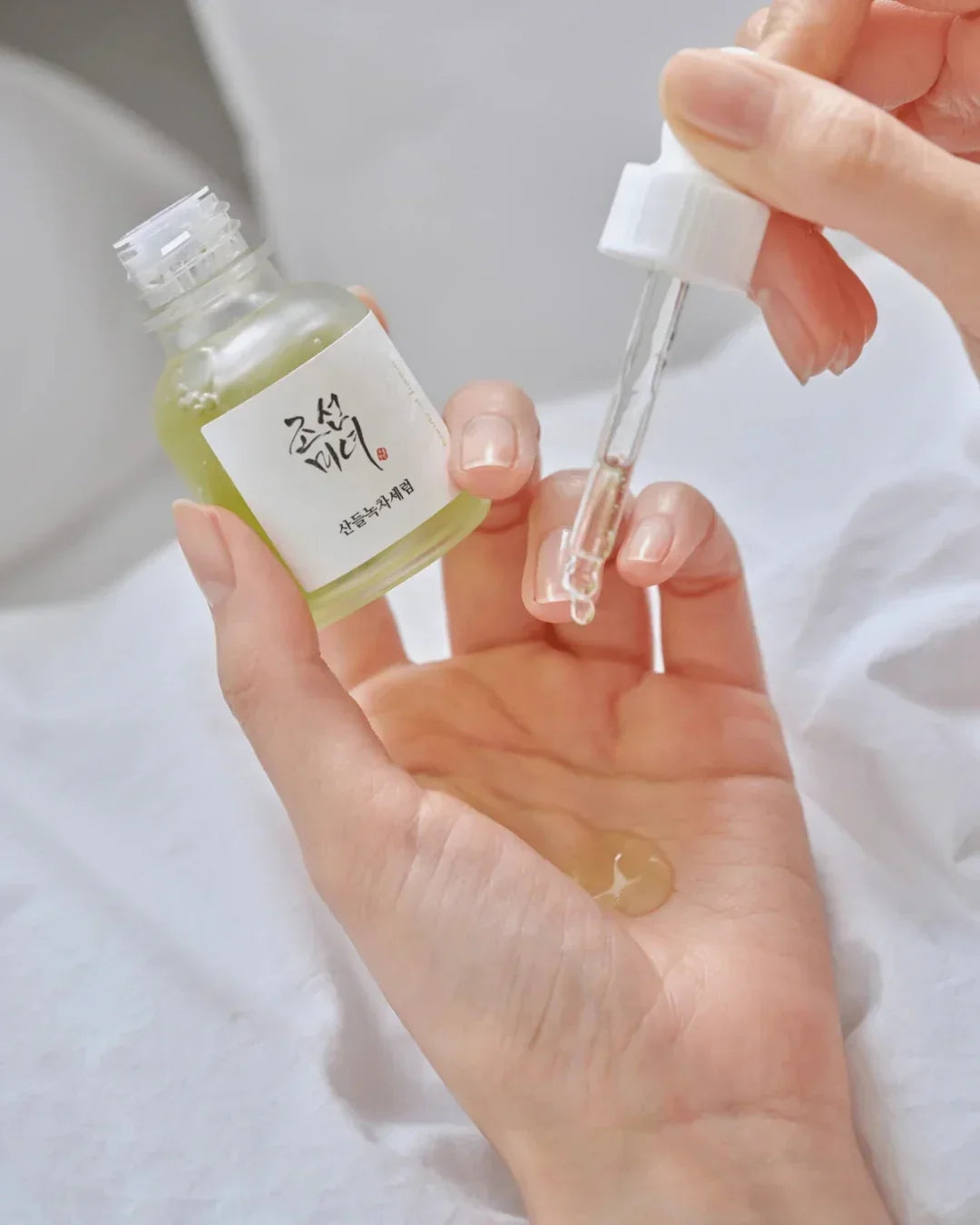 Hand holding a green tea calming serum bottle and dropping serum on palm with a dropper