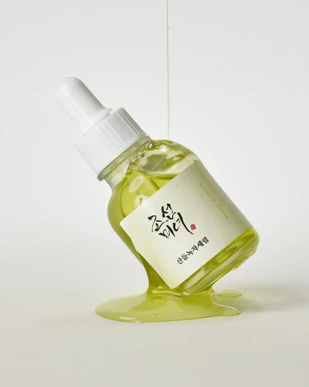 Green tea calming serum bottle with dropper on white surface with spilled green liquid