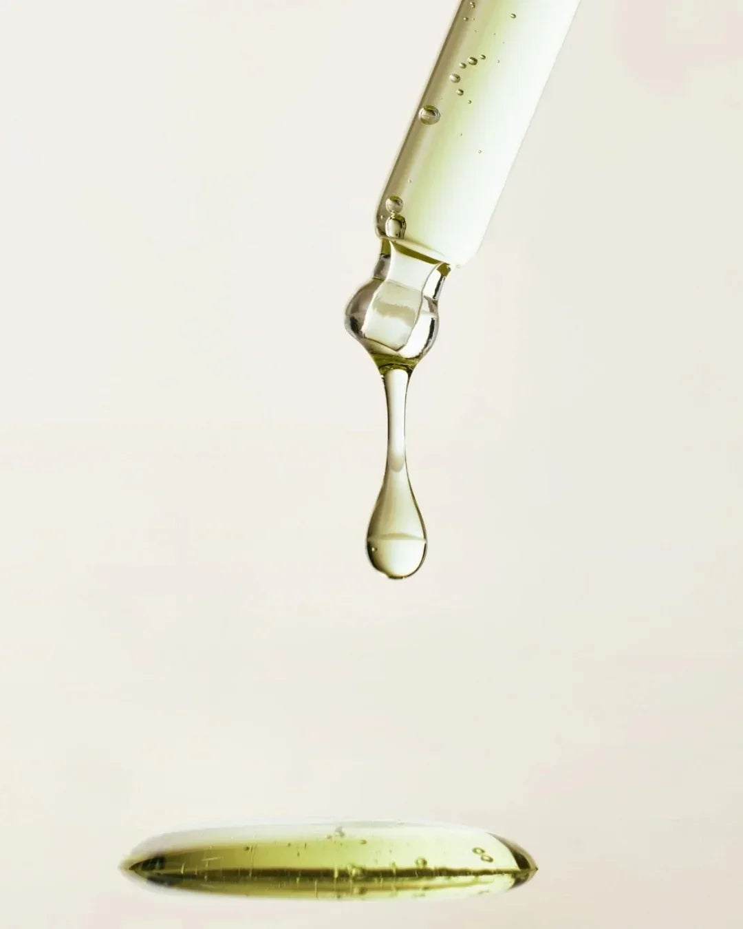 Close-up of green tea calming serum drop falling from glass dropper with clear liquid texture