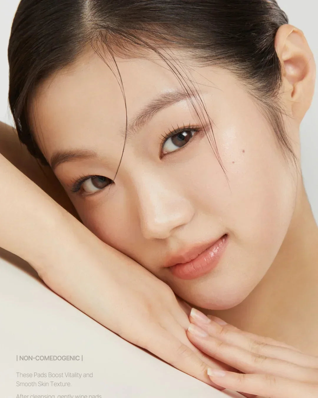 Close-up of a woman with clear, glowing skin resting her face on her hands, showcasing smooth complexion