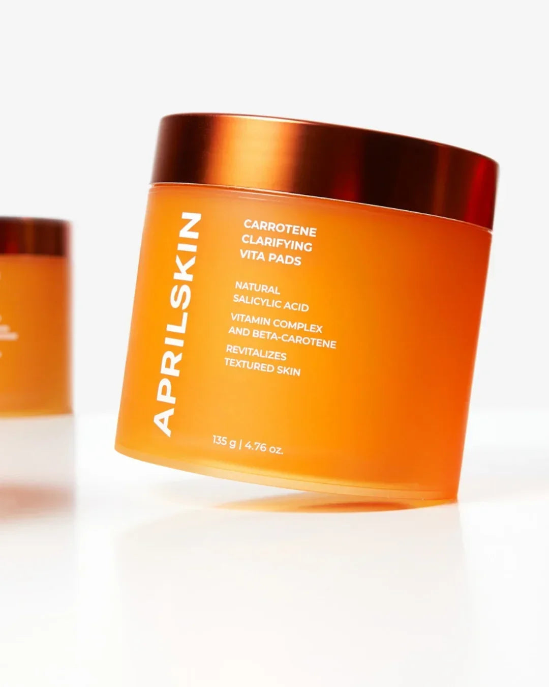 Orange jar of Aprilskin Carotene Clarifying Vita Pads with copper lid on white surface
