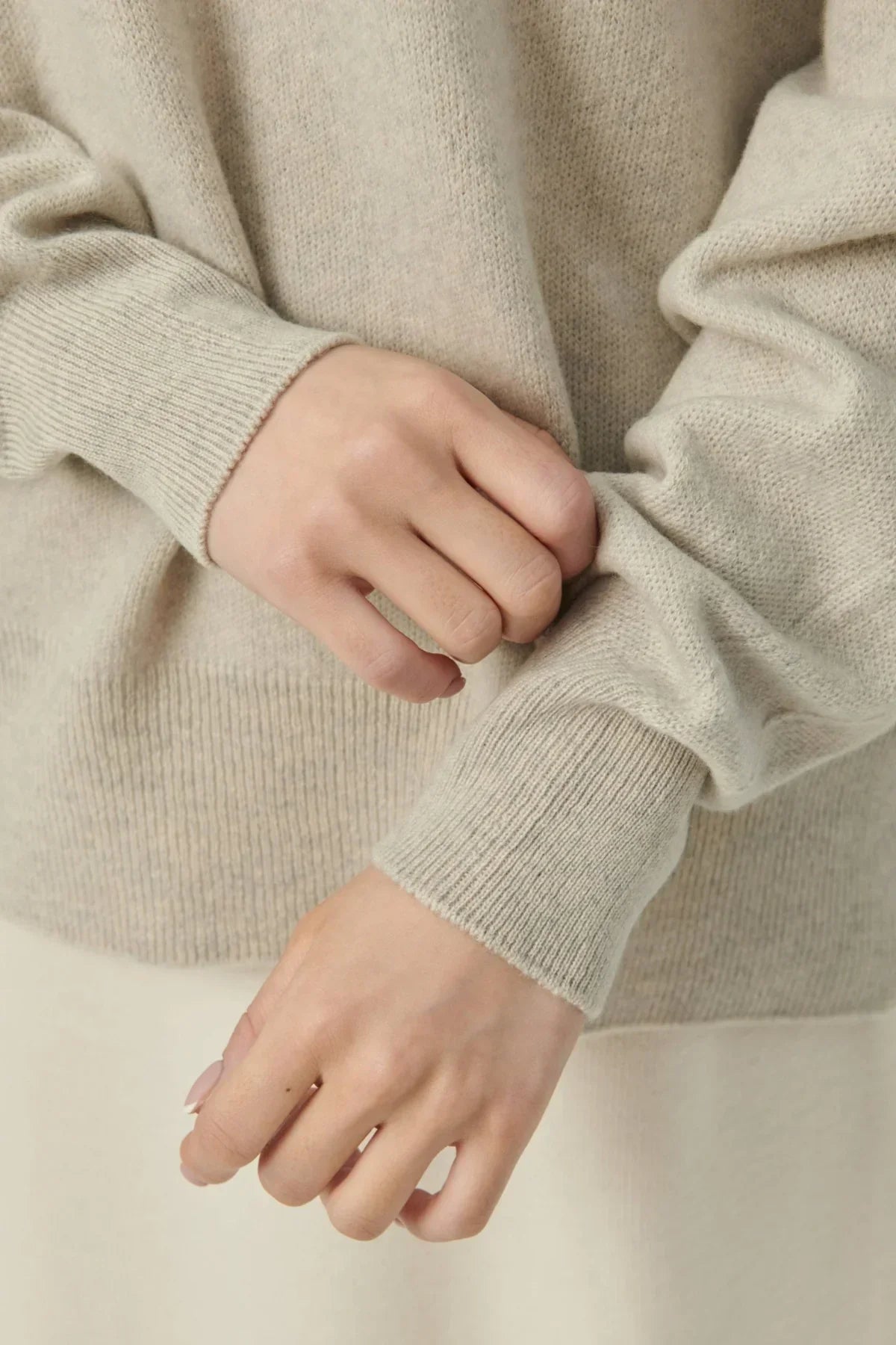 Close-up of hands adjusting beige cashmere sweater sleeve with ribbed cuffs