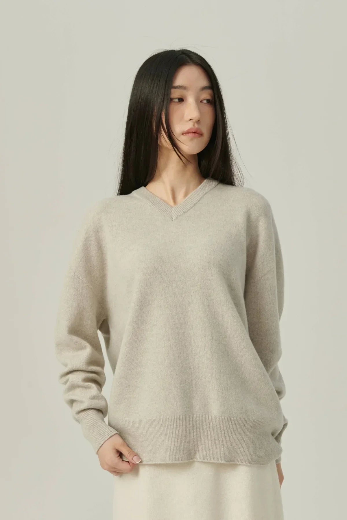 Woman wearing beige cashmere V-neck pullover sweater standing against plain background