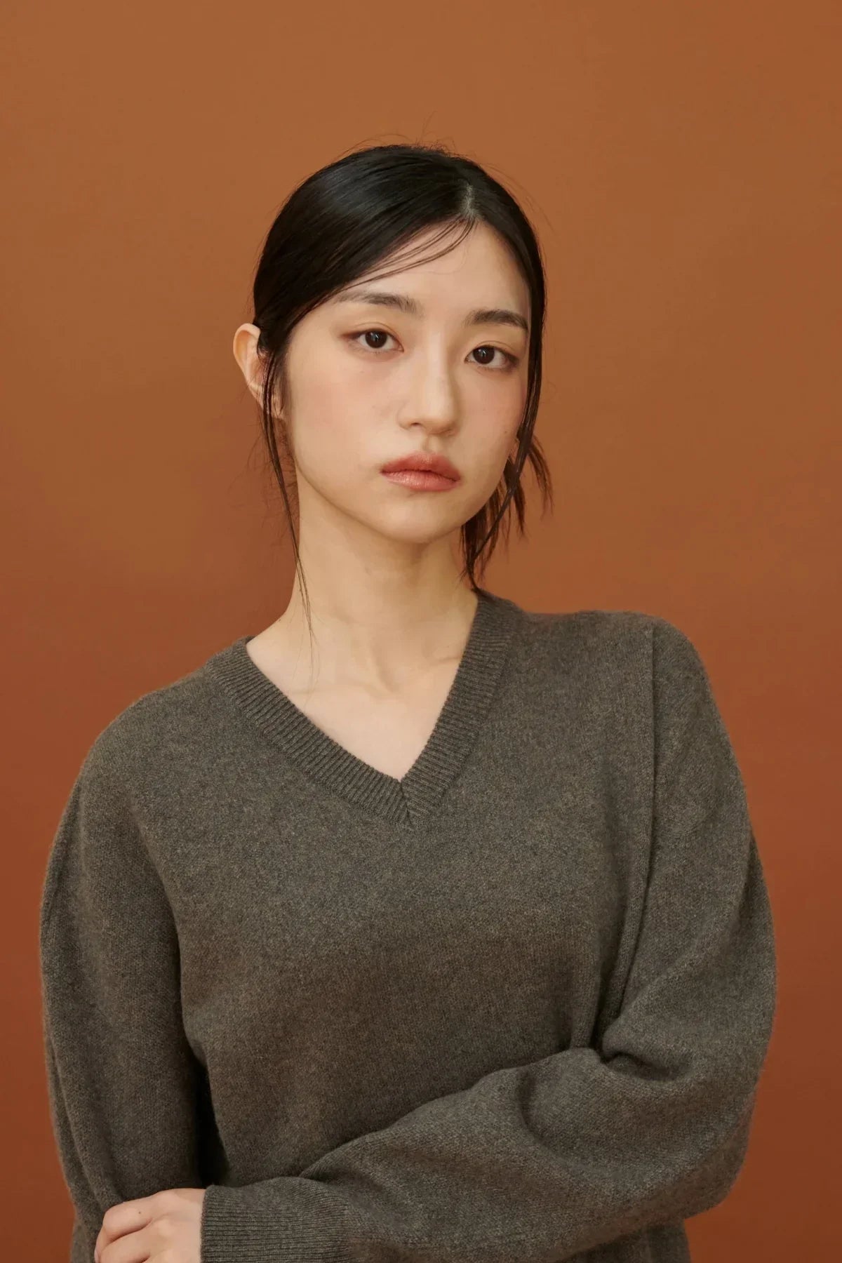 Young woman wearing brown cashmere V-neck pullover against a solid brown background
