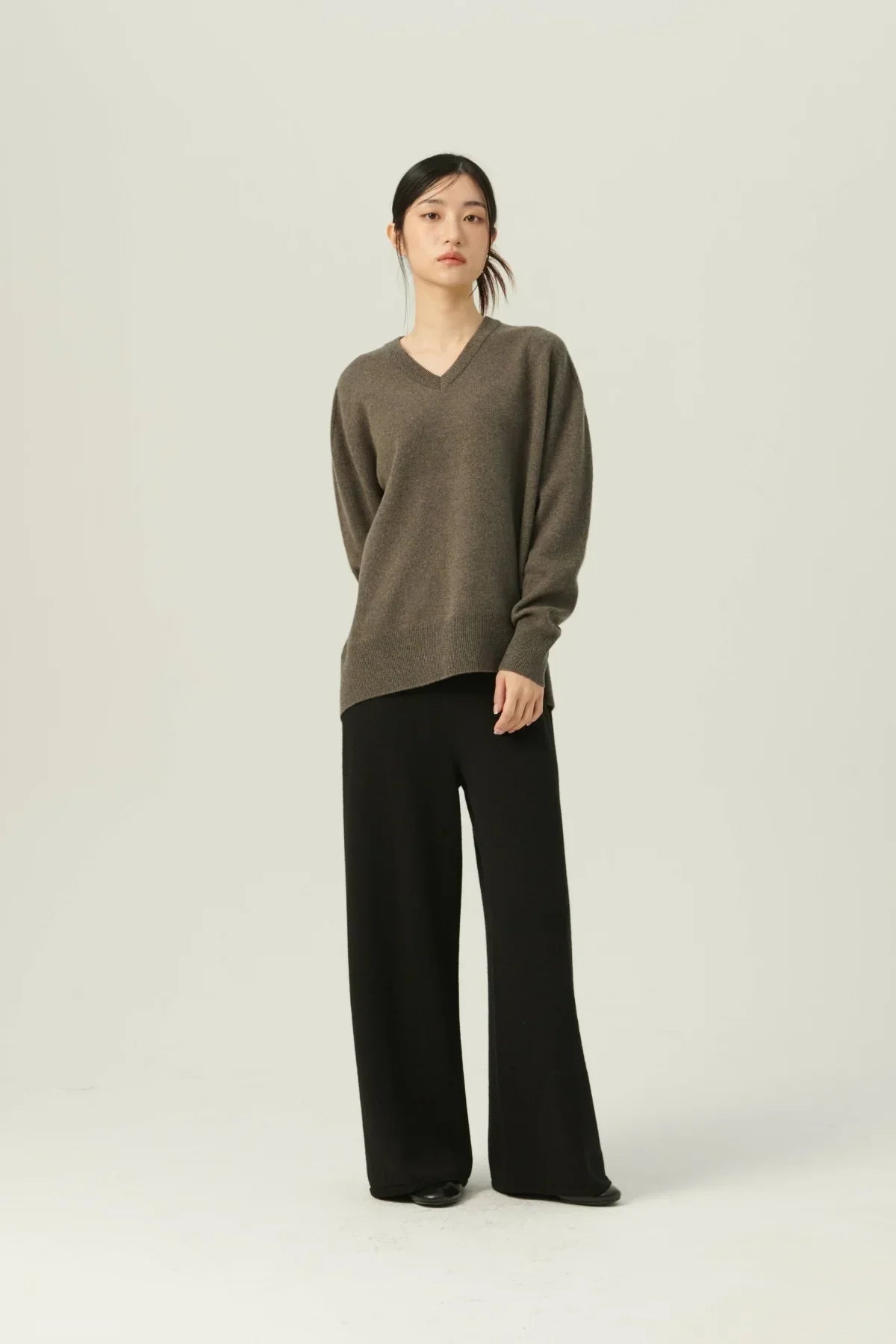 Asian woman wearing brown cashmere V-neck pullover and black wide-leg pants on plain background