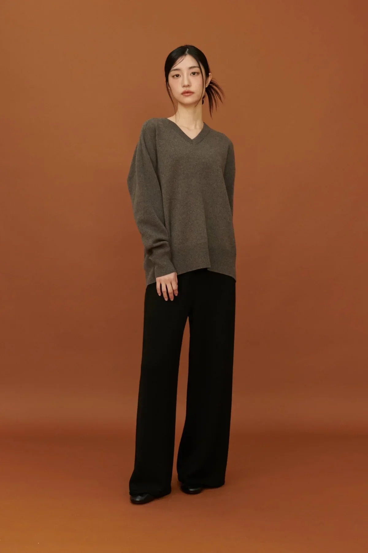 Woman wearing brown cashmere V-neck pullover and black wide-leg pants against brown backdrop