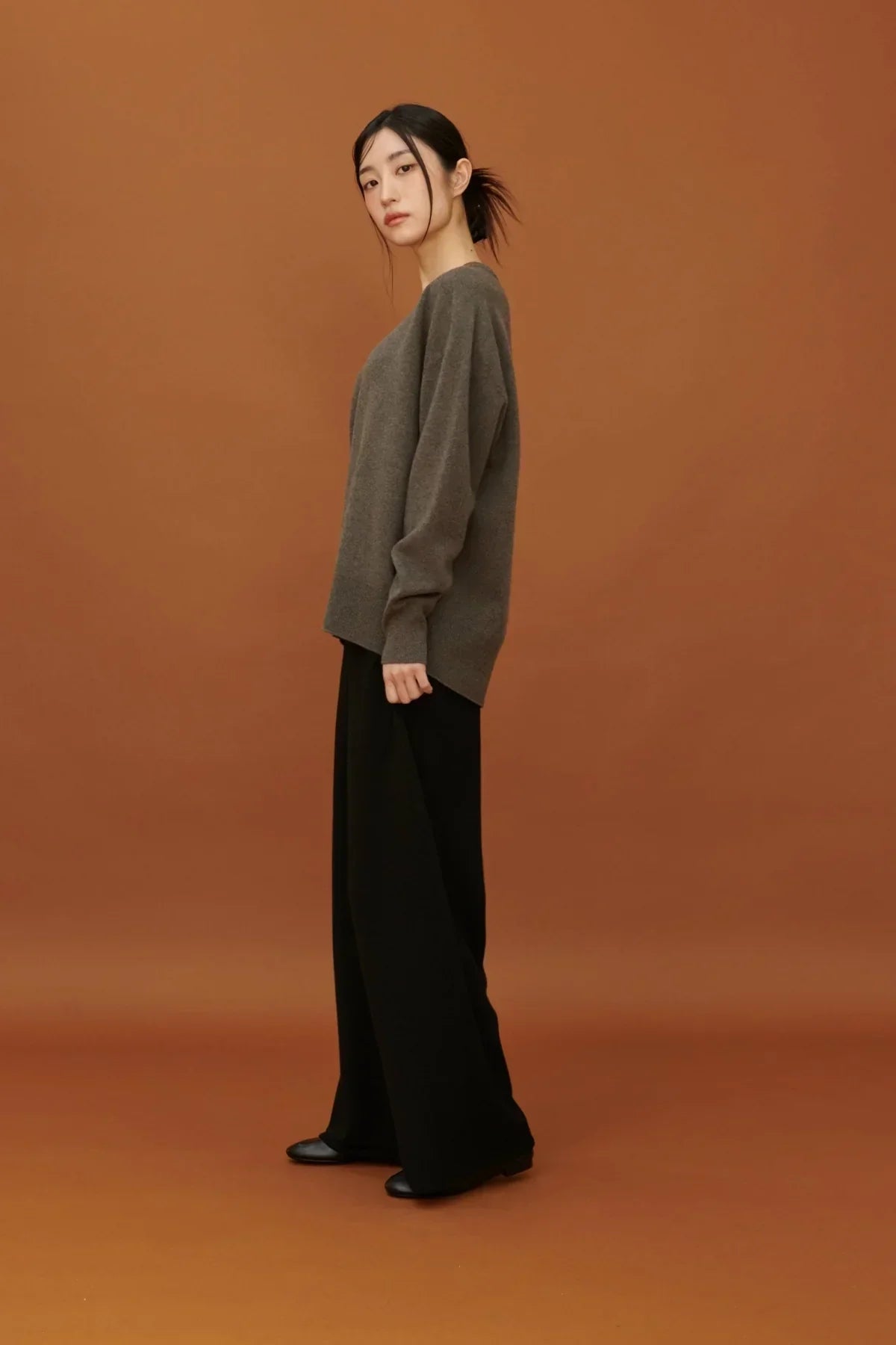 Woman wearing brown cashmere V-neck pullover with black wide-leg pants on brown background