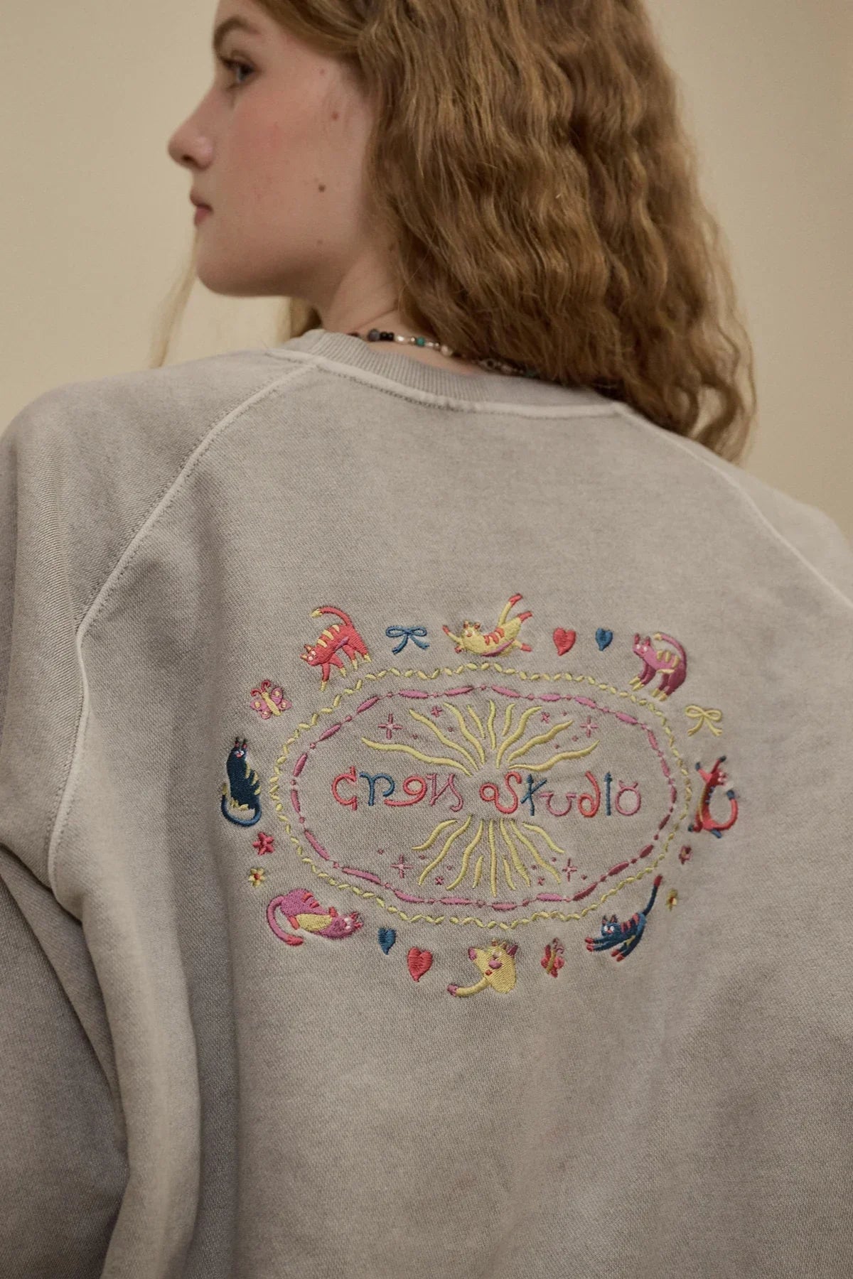 Close-up of a person wearing a gray sweatshirt with colorful cat embroidery on the back