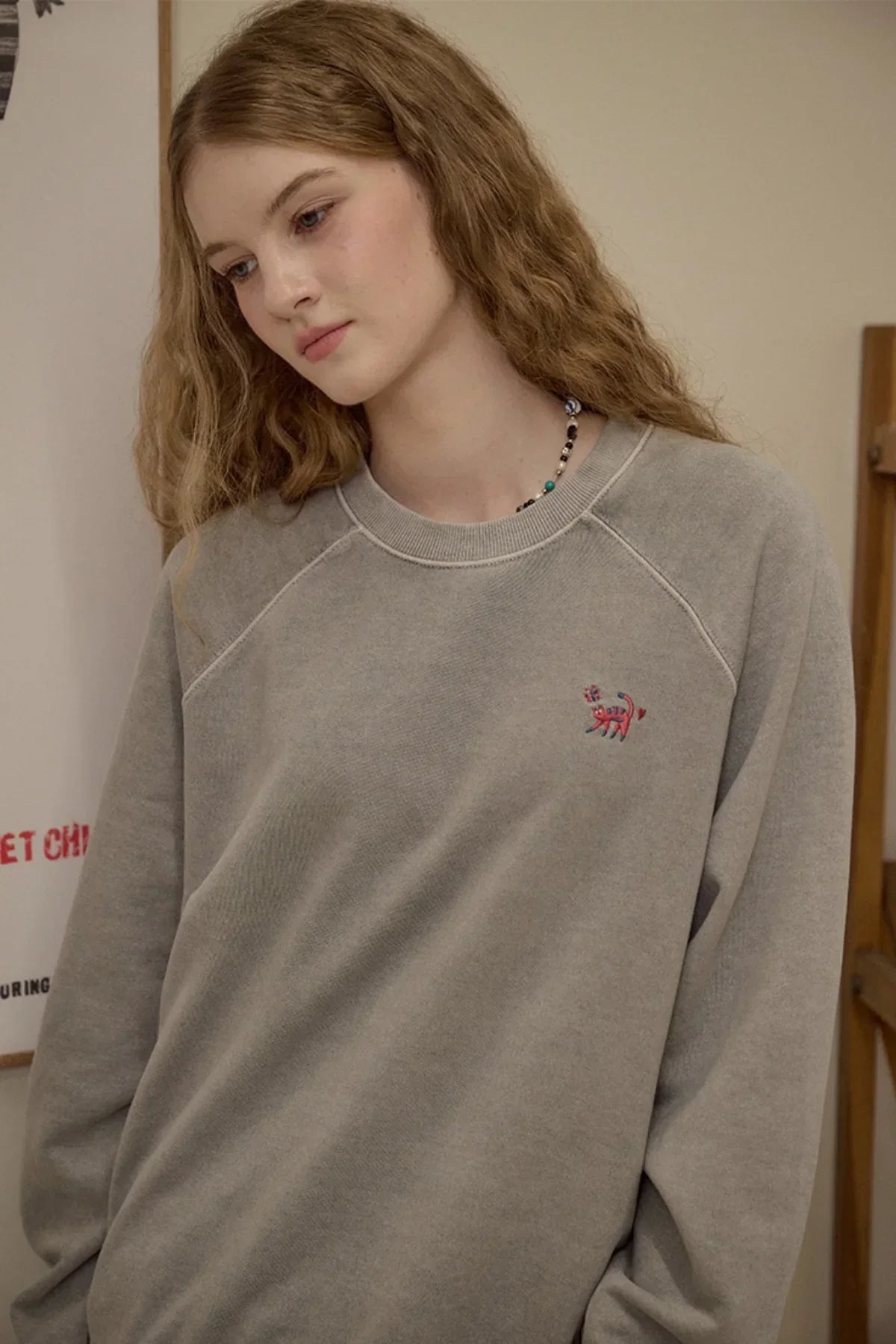 Young woman wearing gray raglan sweatshirt with small red cat embroidery on chest