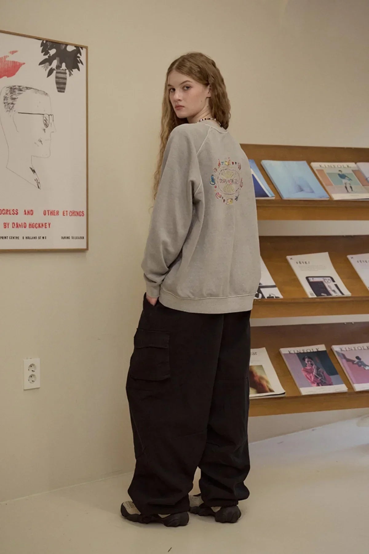 Young woman wearing ghost gray sweatshirt with colorful design and black cargo pants in a gallery